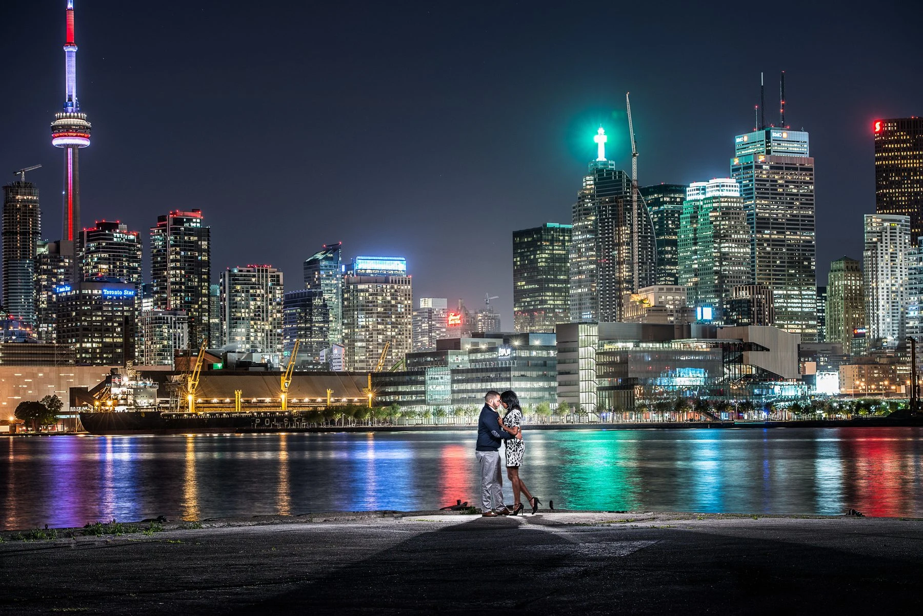 A couple by the water with the illuminated Toronto skyline
