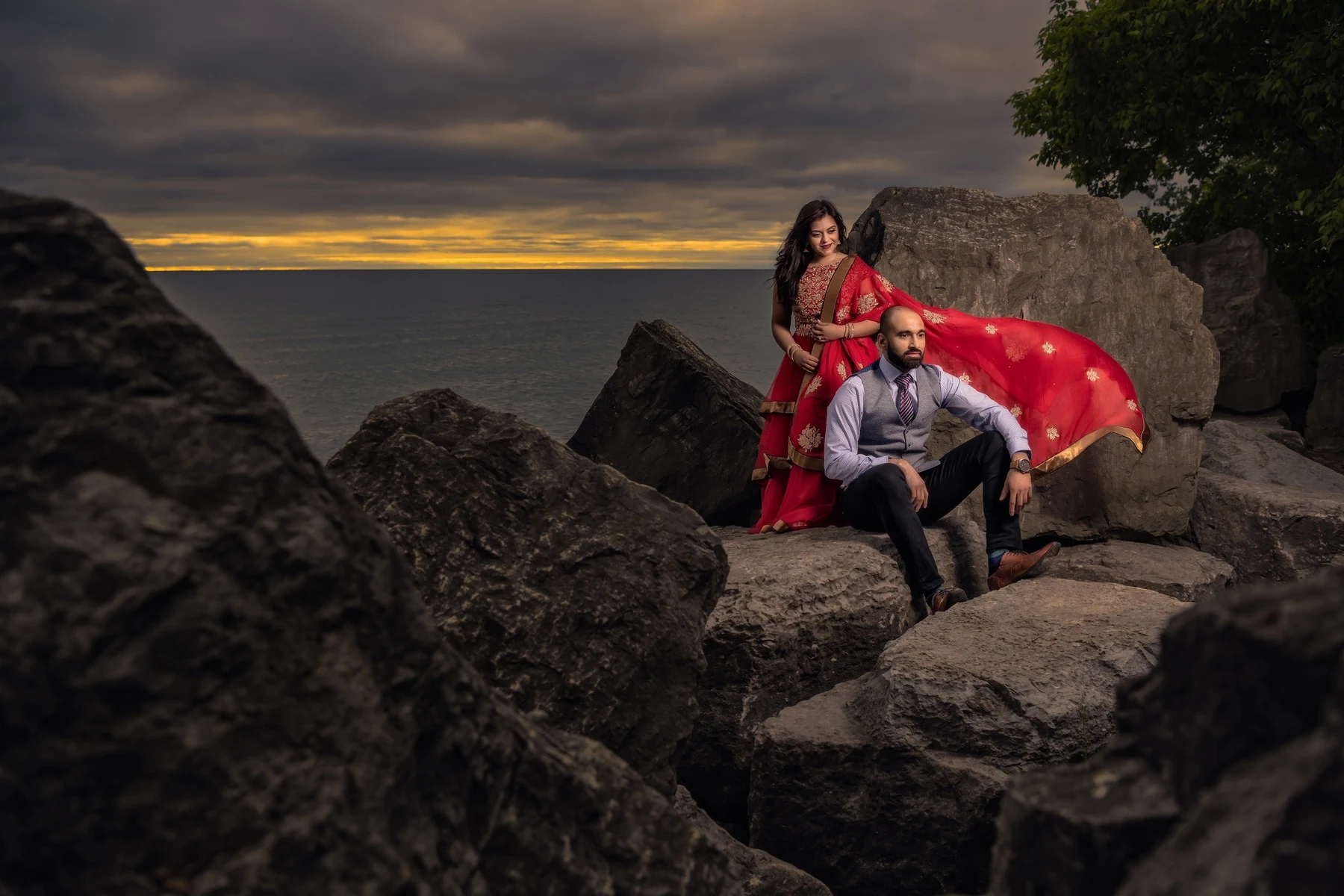 A couple on the rocky shore beneath a golden sunset